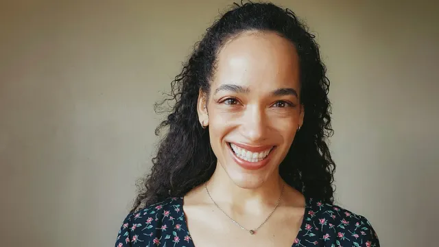 Lächelnde Frau mit Locken vor heller Wand – Trans-Dating