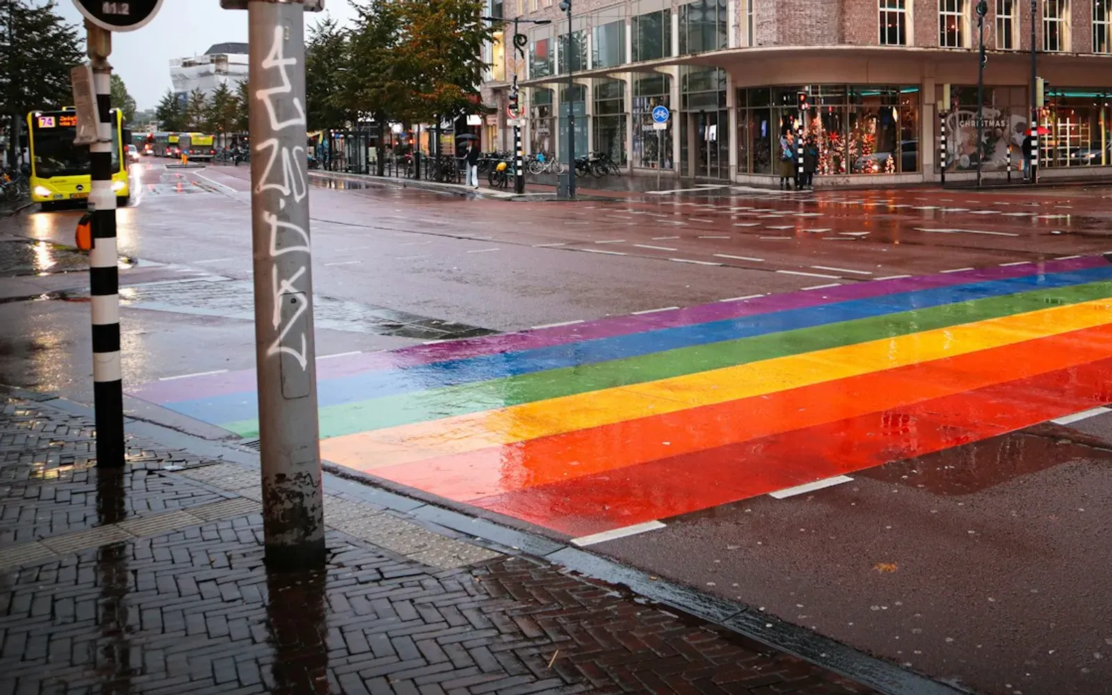 Regenbogenfarbener Zebrastreifen auf nasser Straße in einer Innenstadt